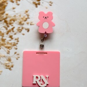 May include: Pink plastic badge holder with a pink bear charm and a white "RN" on a pink background.