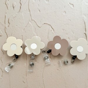 May include: Four flower-shaped retractable badge holders with mirror inserts. Two are beige and two are brown.
