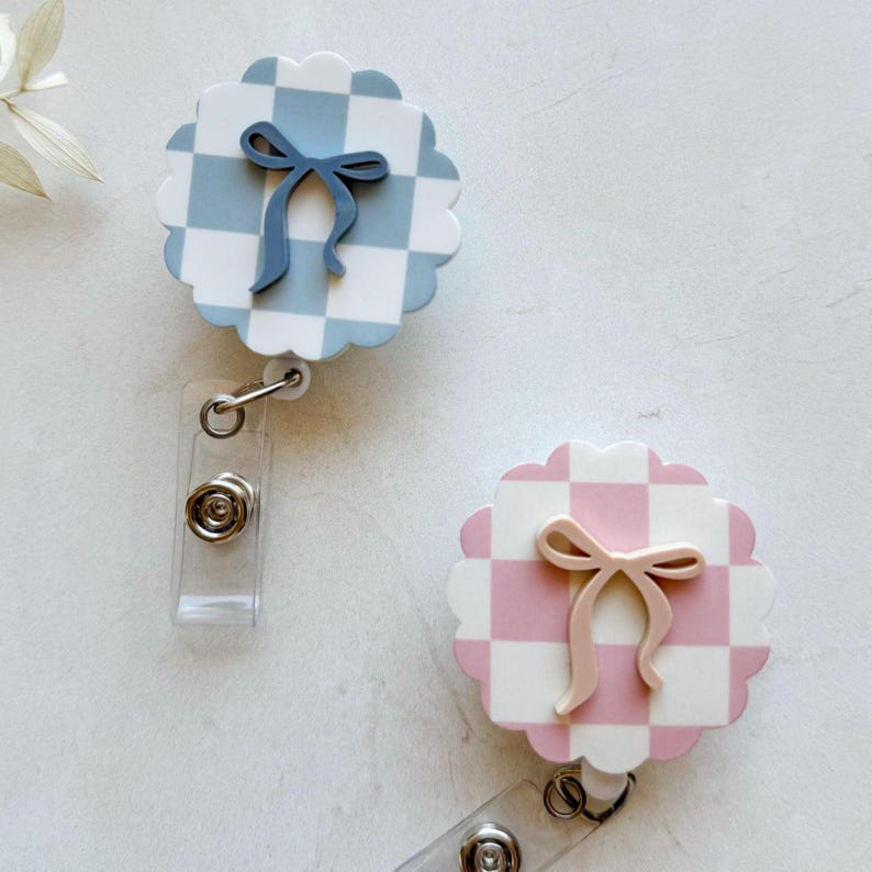 Pu&ograve; includere: Due porta badge con bordo smerlato, motivo a scacchi e fiocco. Uno &egrave; azzurro e bianco con un fiocco blu, l'altro &egrave; rosa e bianco con un fiocco rosa. Ogni porta badge ha un cinturino in plastica trasparente e una clip in metallo.