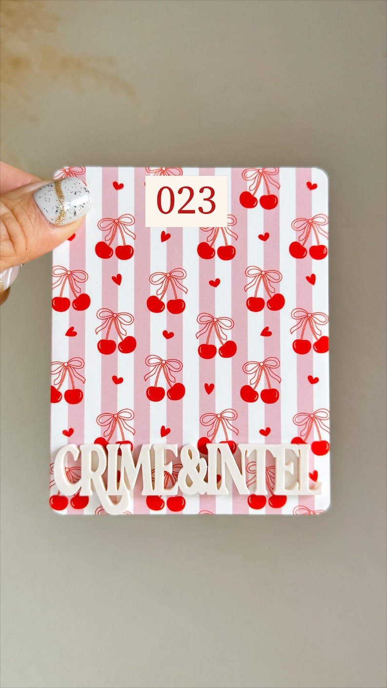 May include: A rectangular, white and pink striped item with a cherry pattern and the text "CRIME & INTEL". The number "023" is in a white box. The cherries are red with a red bow.