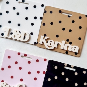 May include: Four name tags with polka dot patterns. The tags are white, tan, pink, and black. The white tag has black dots and the letters "L&D". The tan tag has black dots and the name "Karina". The pink tag has red dots and the name "Sydney". The black tag has tan dots and the word "Radiology".