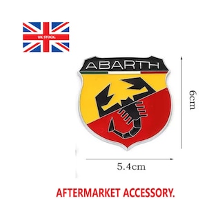 May include: A shield-shaped Abarth emblem featuring a black scorpion on a yellow and red background with the text ABARTH at the top. The emblem measures 6cm in height and 5.4cm in width as indicated by the visible measurement lines and text.