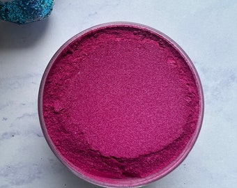 May include: A round container filled with a deep pink, fine-textured powder. The powder has a slight shimmer.