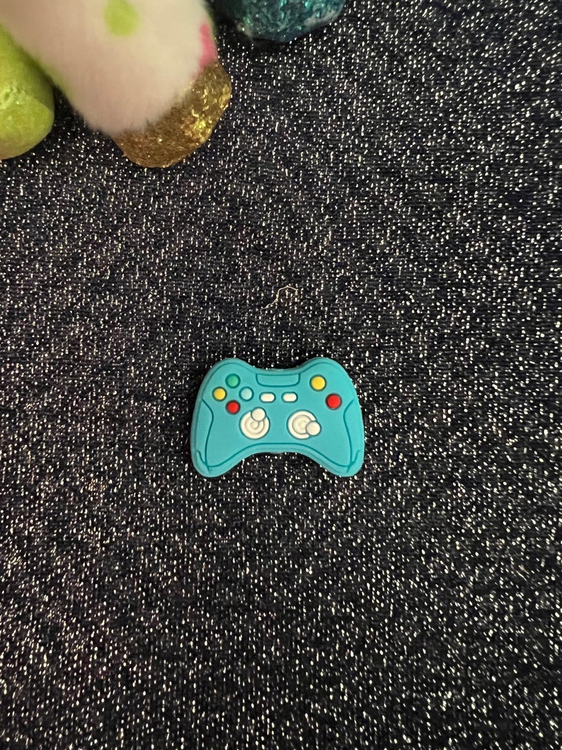 May include: A blue plastic toy video game controller with green, yellow, and red buttons.