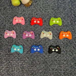 May include: Assortment of ten colorful plastic game controller charms. The charms are in various colors including pink, red, purple, gray, orange, blue, and black.