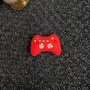 May include: Red plastic game controller charm with white buttons and a black background.