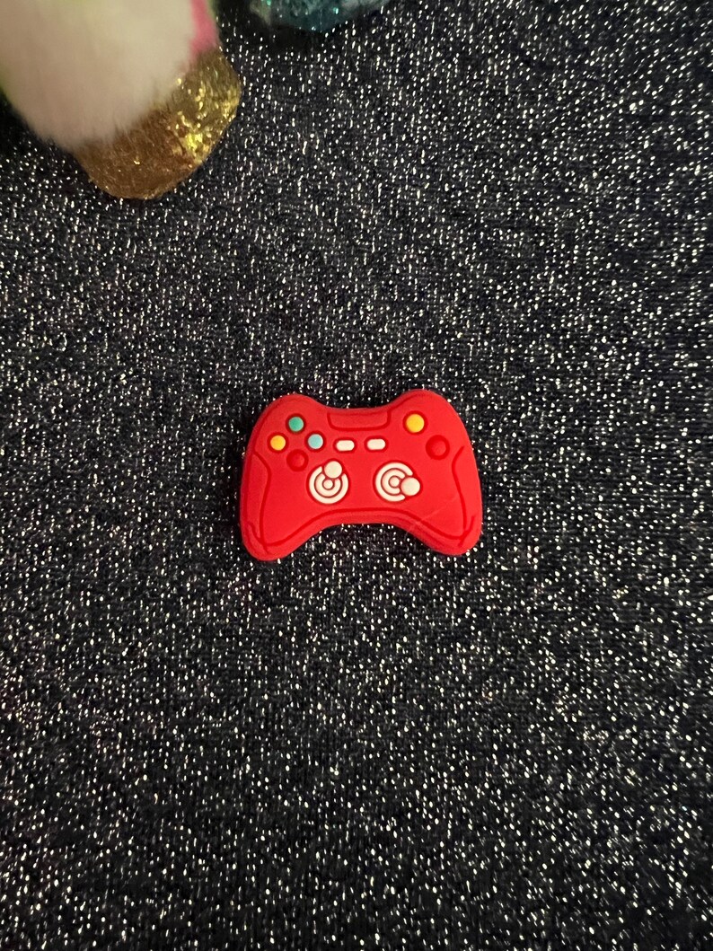 May include: Red plastic game controller charm with white buttons and a black background.