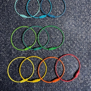 May include: A collection of colorful keychains in shades of blue, green, yellow, orange, and red. Each keychain is a circular loop with a matching clasp. The keychains are arranged on a dark, textured surface.