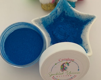 May include: A small jar of cerulean blue glitter with a white lid. The lid has a rainbow unicorn logo and the text "Speckled Unicorn Glitter" and "www.SpeckledUnicornGlitter.com".