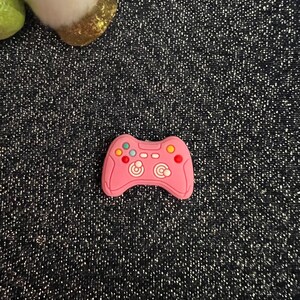 May include: A pink plastic video game controller charm with black and white buttons and a colorful design.