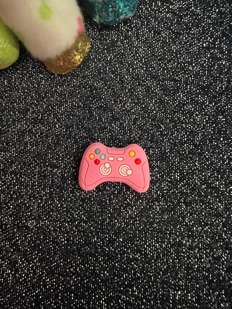 May include: A pink plastic video game controller charm with black and white buttons and a colorful design.