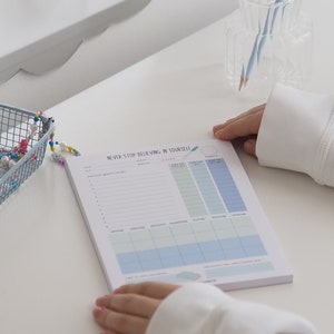 May include: A blue and white planner with the text "NEVER STOP BELIEVING IN YOURSELF" at the top. The planner has sections for daily goals, a weekly schedule, and a monthly calendar.