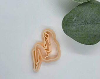 May include: A light orange plastic cookie cutter shaped like a person sitting with legs crossed.