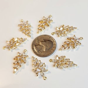 Puede incluir: Ocho abalorios en forma de hoja de color dorado con detalles de cristal transparente. Los abalorios est&aacute;n dispuestos en c&iacute;rculo alrededor de una moneda de veinticinco centavos de d&oacute;lar estadounidense.