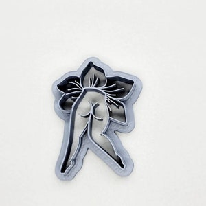 May include: A silver metal cookie cutter in the shape of a stylized human figure with a flower design on the head.