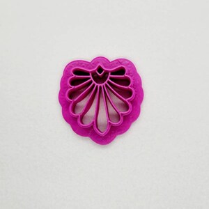 Puede incluir: Un cortador de galletas de plástico rosa en forma de corazón con un diseño de concha decorativo.