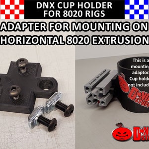 Pode incluir: Adaptador de montagem de suporte de copo preto para plataformas 8020. O adaptador é projetado para extrusão horizontal 8020. A imagem também mostra uma peça preta em forma de cruz com parafusos e um suporte de copo com o texto "D-NUT STUFF".