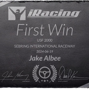 Puede incluir: Placa de pizarra negra grabada con el logo "iRacing" y "First Win". Detalles: "USF 2000", "Sebring International Raceway", fecha y nombre. Presenta un volante y dise&ntilde;o de corona de laurel.