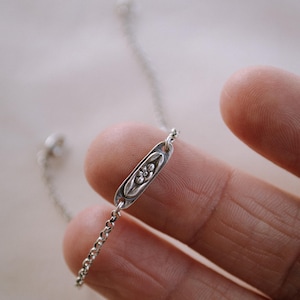 May include: A delicate silver chain bracelet with a small oval charm featuring a floral design.