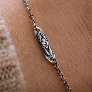 May include: A silver chain bracelet with a small oval charm featuring a floral design.