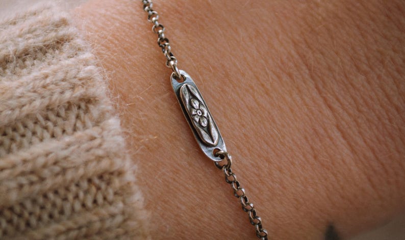 May include: A silver chain bracelet with a small oval charm featuring a floral design.
