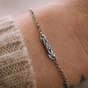 May include: A silver chain bracelet with a small oval charm featuring a floral design.
