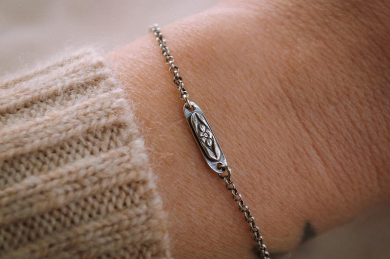 May include: A silver chain bracelet with a small oval charm featuring a floral design.