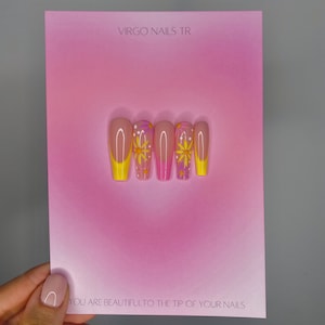 Könnte beinhalten: Ein Set mit fünf pinkfarbenen und gelben Press-on-Nägeln mit einem Blumenmuster. Die Nägel werden auf einer pinkfarbenen Karte mit dem Text "VIRGO NAILS TR" und "YOU ARE BEAUTIFUL TO THE TIP OF YOUR NAILS" präsentiert.