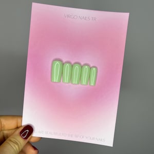Könnte beinhalten: Ein Set mit fünf hellgrünen Press-on-Nägeln mit weißem Umriss. Die Nägel werden auf einer rosa Karte mit dem Text "VIRGO NAILS TR" und "YOU ARE BEAUTIFUL TO THE TIP OF YOUR NAILS" gezeigt.