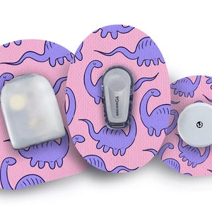 May include: Medical device accessories featuring a pink dinosaur pattern. The set includes a sensor, transmitter, and a round device. These devices are designed for use with a Dexcom G6 continuous glucose monitoring system.