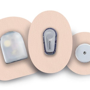 Op de afbeelding: Drie beige kleefpleisters met verschillende ronde en ovale vormen. Elke pleister heeft een klein, wit, rond apparaat bevestigd. Het middelste apparaat heeft de tekst "dexcom G4" erop gedrukt.
