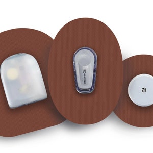 Op de afbeelding: Drie ronde, bruine pleisters met verschillende ronde, witte medische apparaten bevestigd. De apparaten zijn een sensor, een zender en een ontvanger.
