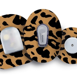 Puede incluir: Tres parches adhesivos redondos, de color marrón y negro con estampado de leopardo, para un dispositivo médico. Los parches tienen un sensor redondo blanco en el centro de cada parche. Un parche tiene una cubierta de plástico transparente sobre el sensor. Otro parche tiene un pequeño dispositivo rectangular gris con el texto "dexcom G6" impreso en él.