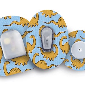 May include: A collection of medical devices with a light blue background featuring a repeating pattern of yellow cartoon dinosaurs. The devices include a white sensor, a gray transmitter, and a white round component.