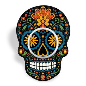 Puede incluir: Un soporte para teléfono con forma de calavera que presenta un fondo negro con un patrón floral y geométrico multicolor. El diseño incluye detalles en naranja, amarillo, azul y verde, con un soporte circular blanco centrado en la frente.