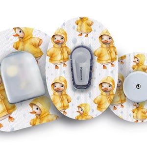 May include: Three round adhesive patches with a white background and a repeating pattern of yellow ducklings wearing yellow raincoats. The center patch has a clear plastic cover with a small hole in the center. The left patch has a clear plastic cover with a small hole in the center. The right patch has a gray plastic cover with a small hole in the center.