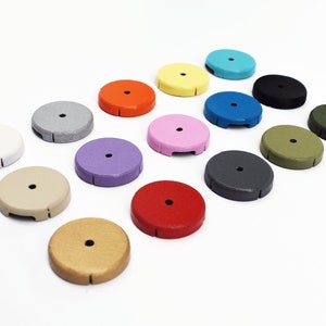 Op de afbeelding: Assortiment van 15 ronde, platte, kleurrijke schijven met een klein gaatje in het midden. De schijven zijn in verschillende kleuren, waaronder wit, grijs, paars, rood, bruin, groen, blauw, roze, zwart en oranje.