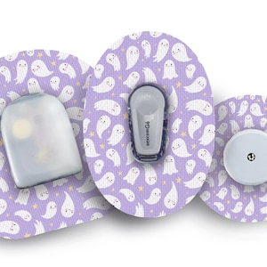 Può includere: Tre cerotti adesivi per dispositivi medici con motivi viola e bianchi con un design a forma di fantasma dei cartoni animati. I cerotti sono per un monitoraggio continuo del glucosio (CGM) e sono decorati con fantasmi bianchi e stelle gialle. Il testo "dexcom G6" è visibile su uno dei cerotti.