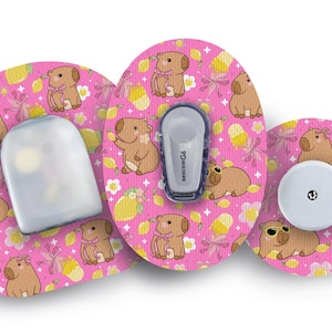 Puede incluir: Un conjunto de tres componentes de dispositivos médicos con un fondo rosa con capibaras de dibujos animados, lazos y limones. Incluye un sensor, un transmisor y un receptor.