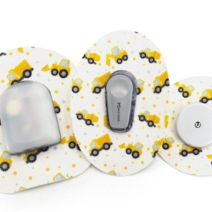 May include: Three round medical patches with a yellow and white construction truck pattern. The patches are different sizes and have a clear plastic cover, a gray sensor, and a white sensor.