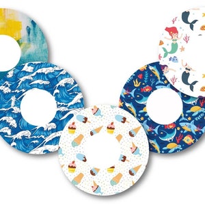 Puede incluir: Conjunto de seis pegatinas redondas de colores con diferentes diseños. Los diseños incluyen un diseño abstracto azul y amarillo, un diseño de olas azules, un diseño blanco con conos de helado y magdalenas, un diseño azul con tiburones y peces, y un diseño blanco con sirenas y peces.