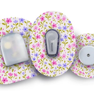Pode incluir: Três adesivos médicos redondos com um padrão floral em rosa, roxo e verde. Os adesivos têm um fundo branco com um pequeno sensor redondo branco no centro de um adesivo. O texto "dexcom G6" está impresso no lado de um sensor branco preso a outro adesivo.