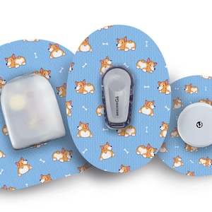 May include: Three round, blue adhesive patches with a repeating pattern of cartoon corgis. The centre patch has a white, round sensor with a black dot in the centre. The patch on the left has a clear, rectangular sensor. The patch on the right has a grey, rectangular sensor with the text "dexcom G6" printed on it.