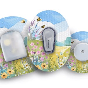 Op de afbeelding: Drie kleurrijke ronde medische apparaatpleisters met een bloemenontwerp. De pleisters hebben een blauwe lucht, groen gras en roze, gele en paarse bloemen. Eén pleister heeft een kleine witte sensor met het woord "Dexcom" erop gedrukt. Een andere pleister heeft een kleine ronde witte sensor. De derde pleister heeft een kleine ronde witte sensor met een klein zwart stipje in het midden.