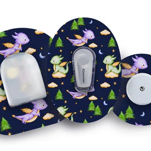 May include: A set of medical devices with a whimsical dragon pattern. The devices include a sensor, transmitter, and receiver, all adorned with a navy blue background, featuring green and purple dragons, clouds, trees, stars, and moons.