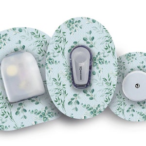 Puede incluir: Tres parches médicos redondos con un patrón de hojas verdes y azules. El parche del centro tiene un pequeño círculo blanco con un punto negro en el centro. El parche de la izquierda tiene un pequeño dispositivo de plástico transparente con una pequeña luz en su interior. El parche de la derecha tiene un pequeño dispositivo gris con el texto "dexcom G6" impreso en él.