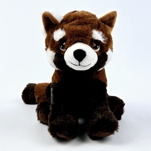 May include: A plush red panda stuffed toy with brown fur, white facial markings, and black paws. The red panda is sitting with its legs crossed and its head tilted slightly to the side.