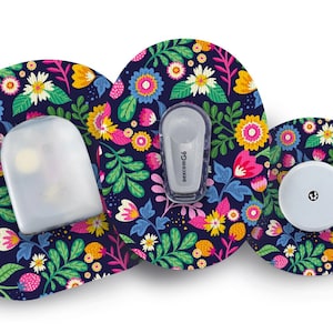 May include: Three round adhesive patches with a floral pattern in shades of pink, yellow, green, and white on a dark blue background. The patches are designed to cover medical devices. One patch has a clear plastic cover, another has a small white device with the text "dexcom G6" printed on it, and the third has a small white round button.