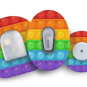 Könnte beinhalten: Drei runde, farbige, selbstklebende Pflaster mit einem Regenbogen-Pop-it-Design. Die Pflaster sind dazu bestimmt, medizinische Geräte abzudecken. Ein Pflaster hat eine transparente Plastikabdeckung, ein anderes hat ein weißes, rundes Gerät mit einem schwarzen Punkt und das dritte hat ein weißes, rechteckiges Gerät mit dem Text "dexcom G6".