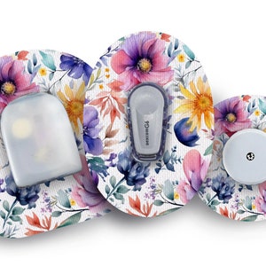 Op de afbeelding: Drie ronde pleisters met een aquarel bloemenpatroon in tinten roze, paars, blauw en geel. Eén pleister heeft een transparant plastic reservoir, een andere heeft een witte insulinepomp en de derde heeft een witte ronde sensor.